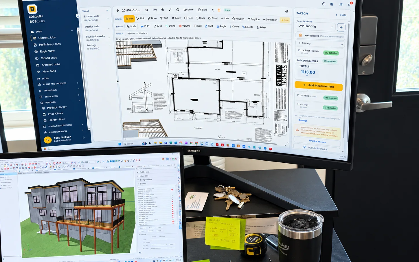A desk with BOS open on a plan takeoff on the monitor and a 3D model of the house on a laptop, a tape measure and a BOS.build tumbler beside them