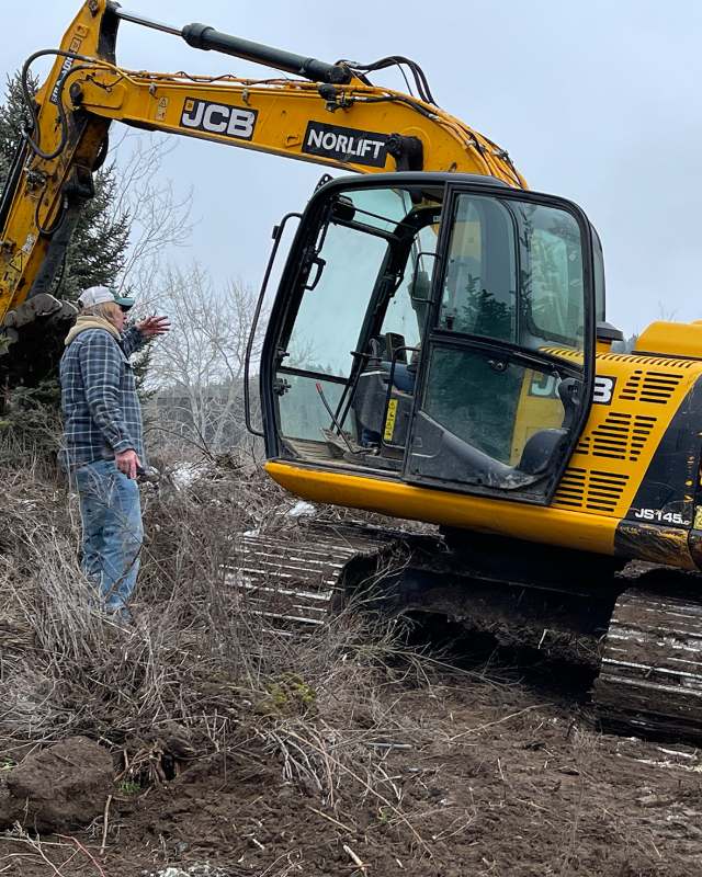 Excavator clearing a lot on a North Idaho jobsite, superintendent directing the operator.