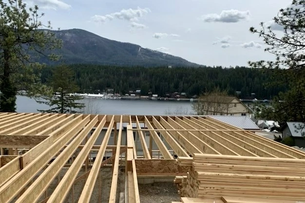 Roof trusses going up on a Sullivan Homes job above a lake, with mountains behind