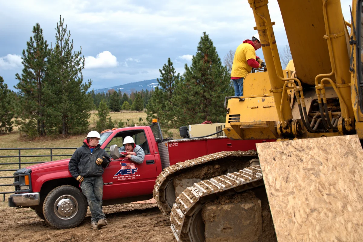 An excavation crew talking at their pickup beside a tracked excavator on a job site
