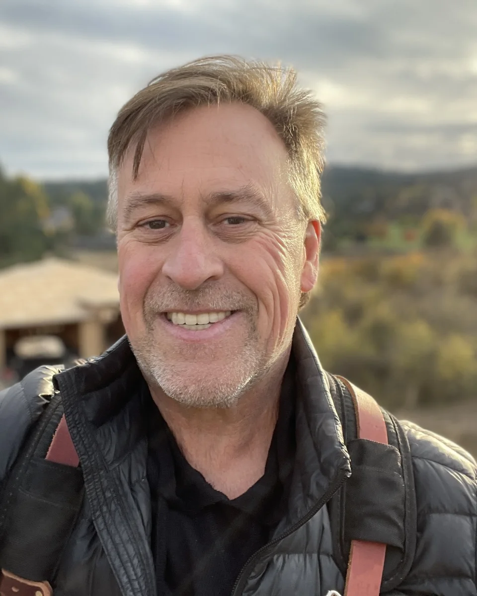 Todd Sullivan outdoors on a job, smiling, a house under construction behind him