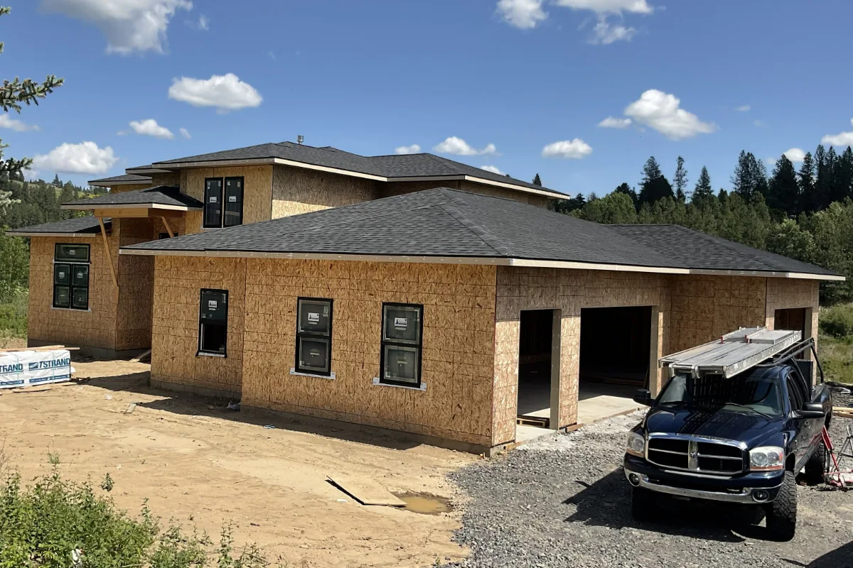 A Sullivan Homes truck in front of a house under construction: sheathed, roofed, windows in